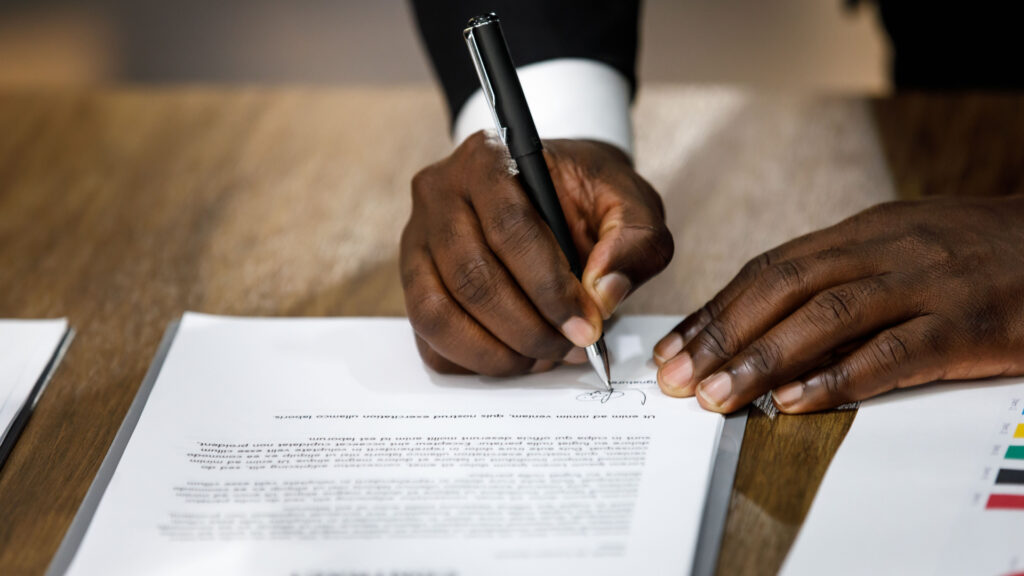 Zoom sur les mains d'une personne qui signe un contrat de travail (salariat) à l'aide d'un stylo noir.